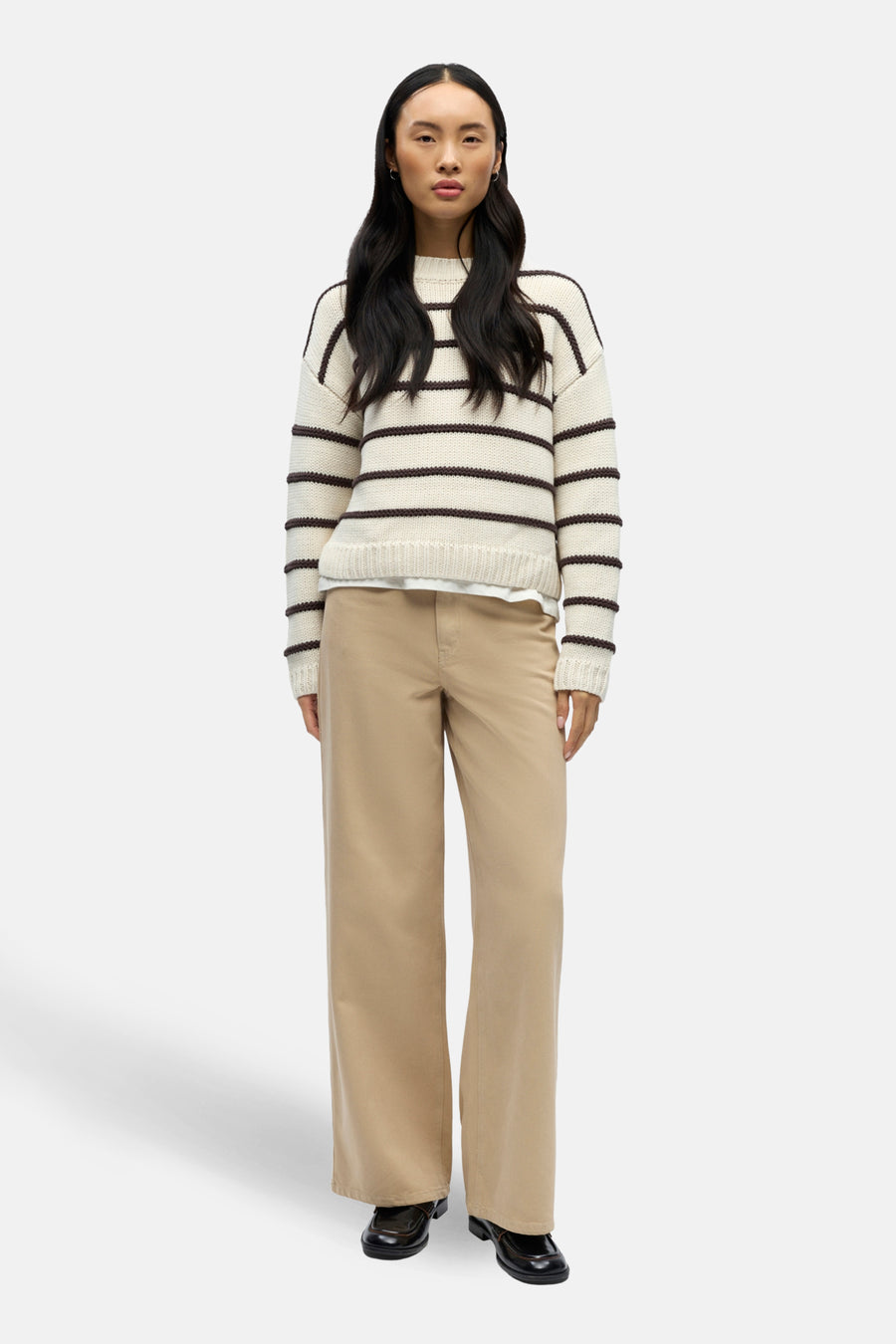 Gilet rond encolé écru d'OBJECT, avec des rayures brunes, porté avec un pantalon beige et des chaussures noires.