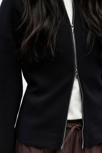 Zwart vest met zilveren rits, wit shirt, bruine broek.