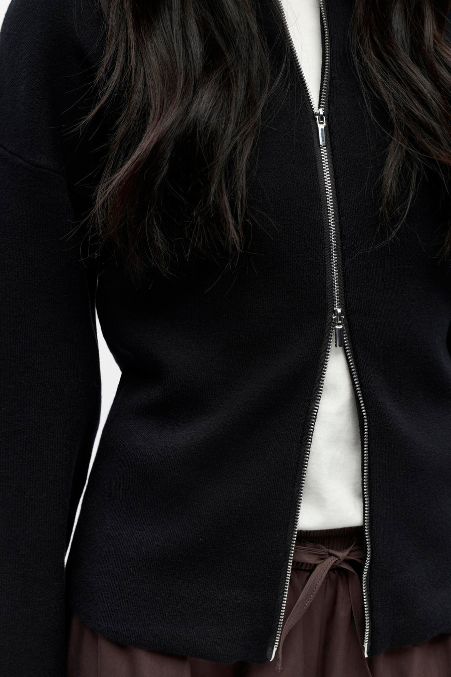 Zwart vest met zilveren rits, wit shirt, bruine broek.