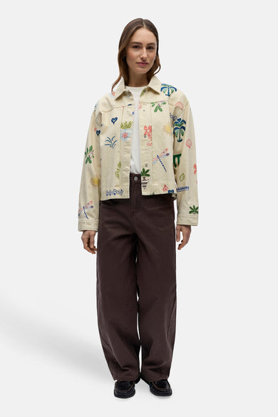 Korte beige jas van OBJECT, met kleurrijke tropische print en gedragen met een wit T-shirt en bruine wijde pijpen broek.
