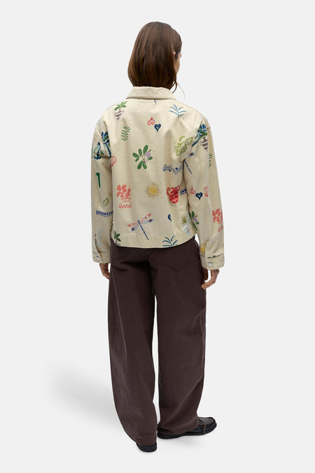 Korte beige jas van OBJECT, met een opvallende print met diverse motieven, gecombineerd met bruine broeken en zwarte schoenen.