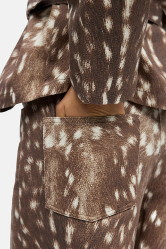 Bruine broek en jas met witgespikkelde print, hand in zak.