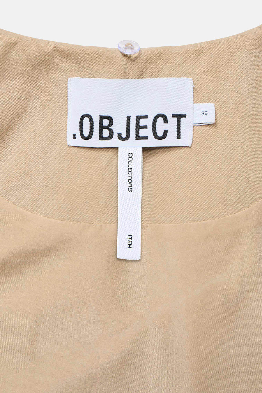 Manteau court beige de OBJECT, avec une étiquette blanche à texte noir et un bouton en plastique sur le dessus.
