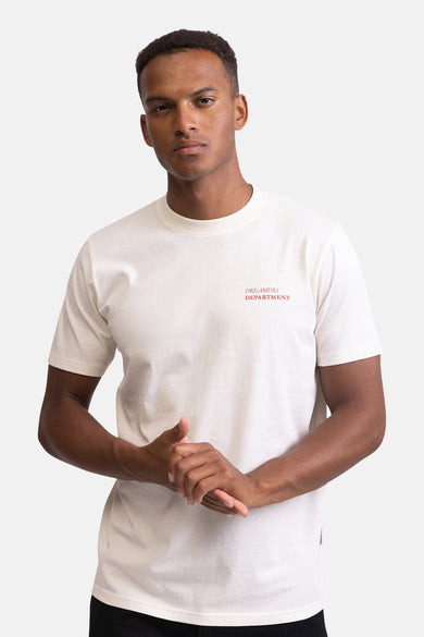 Man met roomkleurig T-shirt met opdruk "Dreamers Department" tegen een witte achtergrond.
