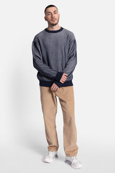 Blauwe trui met ronde hals van REDEFINED REBEL, met verticale strepen, gedragen met corduroy broek en witte sneakers.
