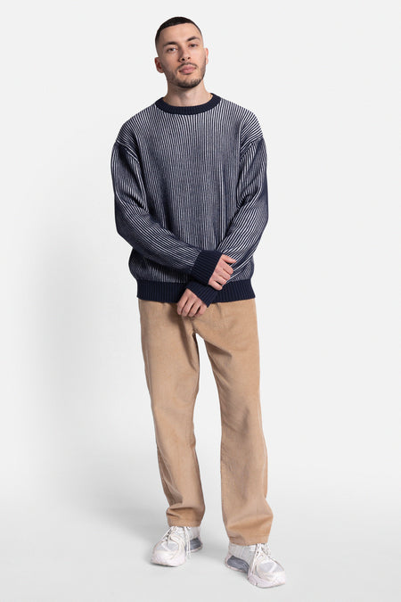 Blauwe trui met ronde hals van REDEFINED REBEL, met verticale strepen, gedragen met corduroy broek en witte sneakers.
