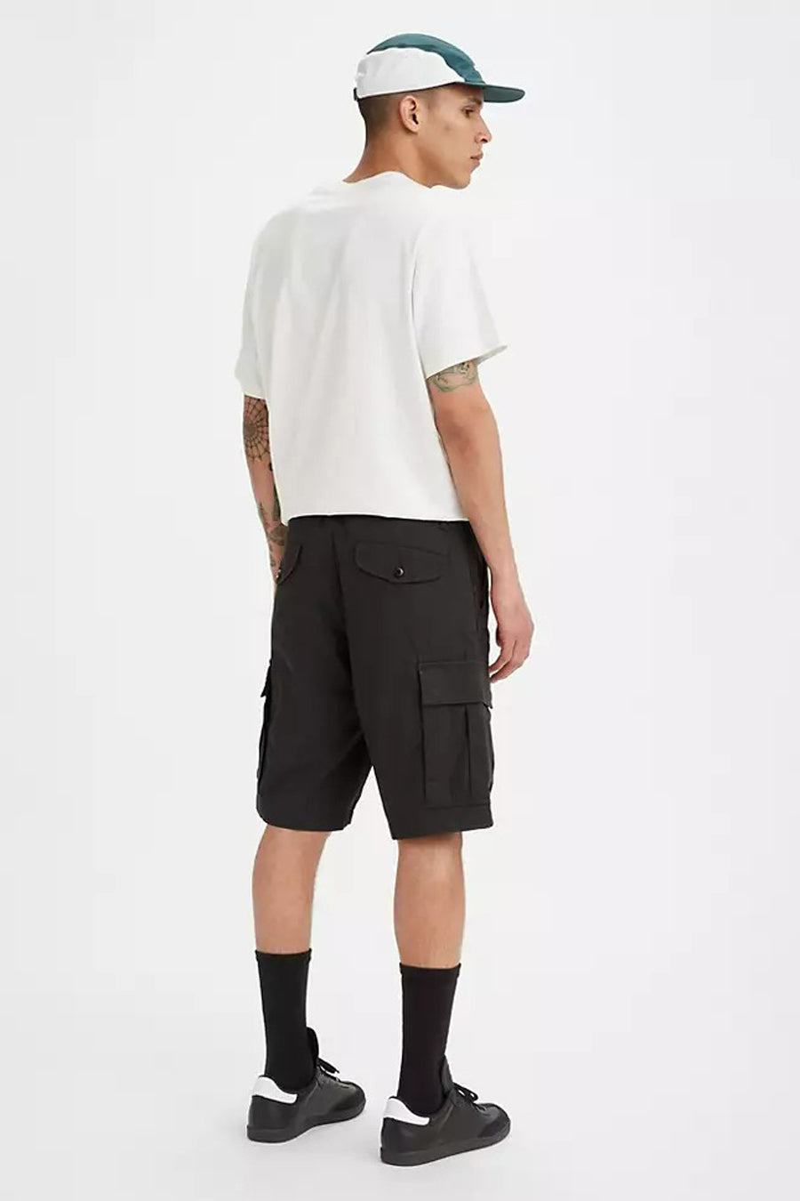 Man van achteren gezien, witte top, zwarte cargoshorts, zwarte sokken, zwarte sneakers, witte pet.