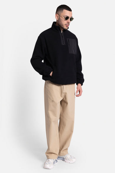 Beige broek van REDEFINED REBEL, met wijde pijpen en gecombineerd met een zwarte fleece trui en witte sneakers.