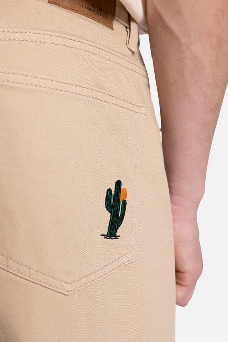 Beige broek van REDEFINED REBEL, met geborduurde cactus op de achterzak.
