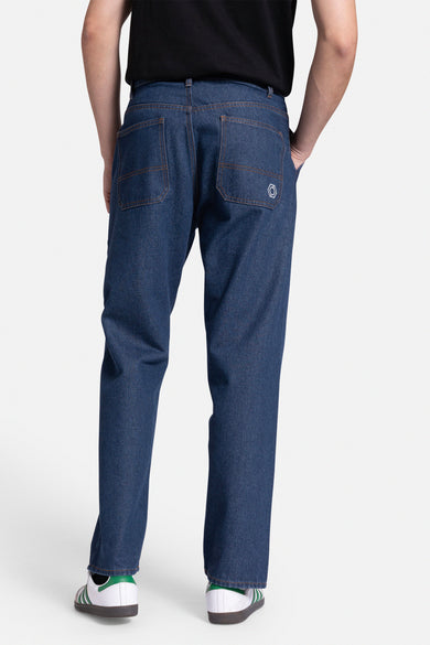 Donkerblauwe straight jeans van REDEFINED REBEL, met achterzakken en gedragen met witte sneakers met groene details.
