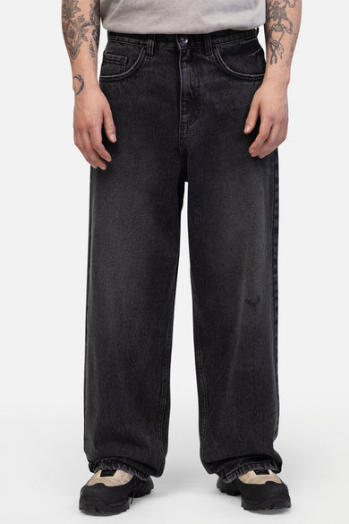 Donkergrijze wijde jeans van REDEFINED REBEL, met een kleine beschadiging op het rechterbeen en zwarte schoenen.
