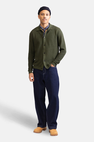 Wijde jeans in donkerblauw denim van REDEFINED REBEL, met witte stiksels, gedragen met een groene cardigan en bandana.
