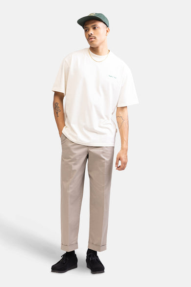 T-shirt écru à manches courtes de REDEFINED REBEL, avec une subtile impression textuelle et porté avec un chapeau vert et une chaîne dorée.
