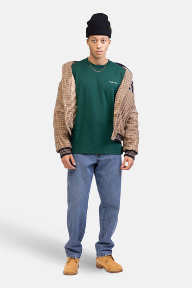 T-shirt vert avec manches courtes de REDEFINED REBEL, porté sur les épaules et associé à une chaîne d'or et des jeans bleus.