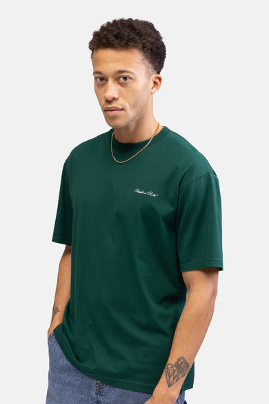 T-shirt vert avec manches courtes de REDEFINED REBEL, avec un petit logo sur la poitrine, porté avec une chaîne d'or.