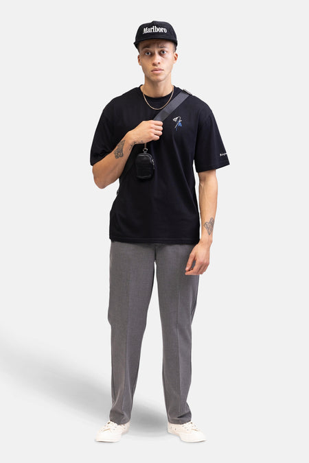 Zwart T-shirt met korte mouwen van REDEFINED REBEL, met geborduurd bloemmotief en gedragen met een pet en grijze pantalon.
