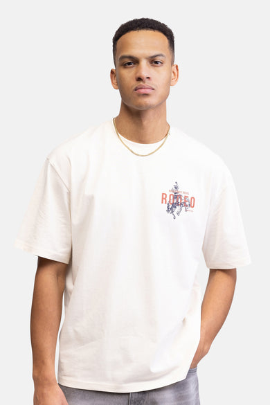 T-shirt écru à manches courtes de REDEFINED REBEL, imprimé "RODEO REBEL", associé à un bandana rouge et des jeans gris.