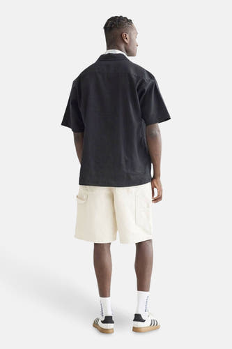 Zwart hemd met korte mouwen van WOODBIRD, gezien van achteren, met crèmekleurige shorts en sportschoenen.