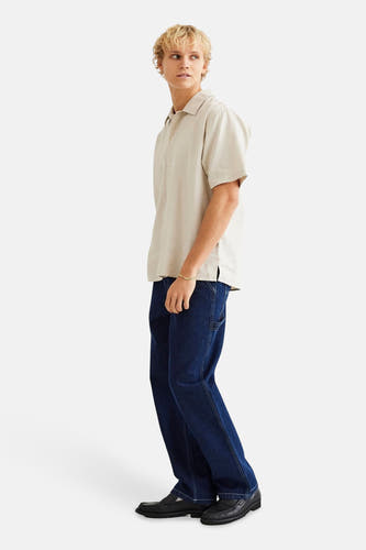 Chemise beige à manches courtes de WOODBIRD, portée avec des jeans bleus foncés et des loafers noirs.