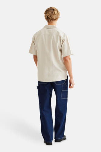 Chemise beige à manches courtes de WOODBIRD, vue de derrière, associée à des jeans bleus foncés et des chaussures noires.