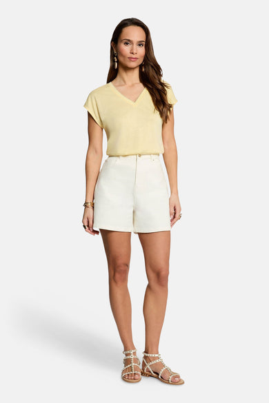 Geel T-shirt van Morgan De Toi met v-hals en korte mouwen, gedragen met crèmekleurige shorts en gouden sandaaltjes.