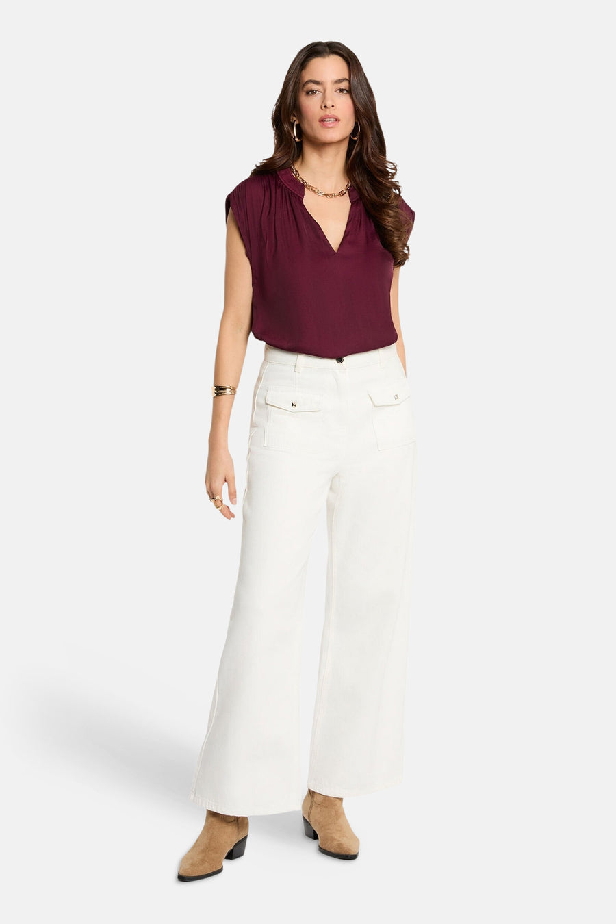 Mouwloze bordeaux blouse van Morgan De Toi, met een V-hals en gecombineerd met witte broek en bruine laarsjes.