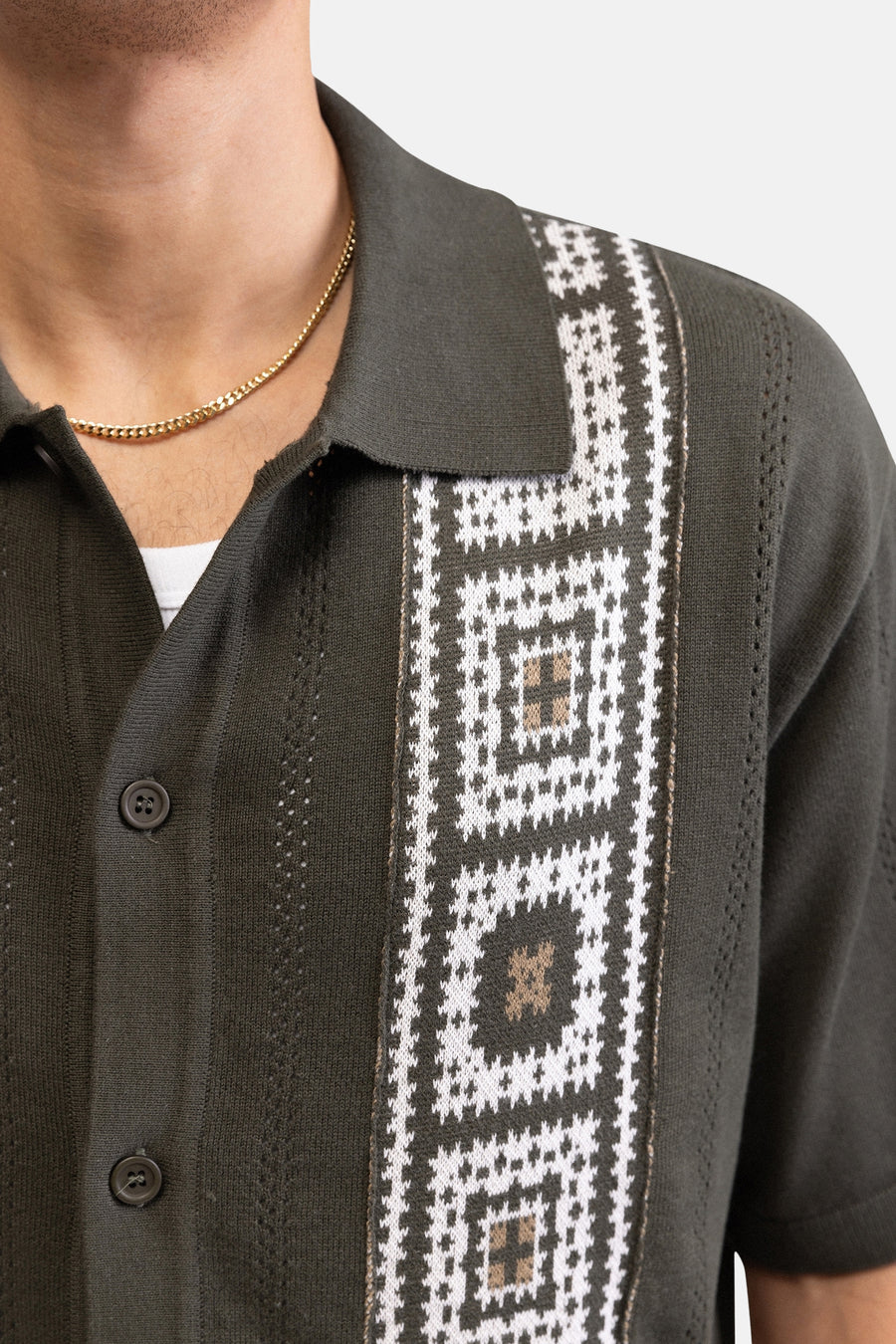 Groen gebreid hemd met korte mouwen van REDEFINED REBEL met wit en beige geometrisch patroon, polo kraag en gouden ketting.