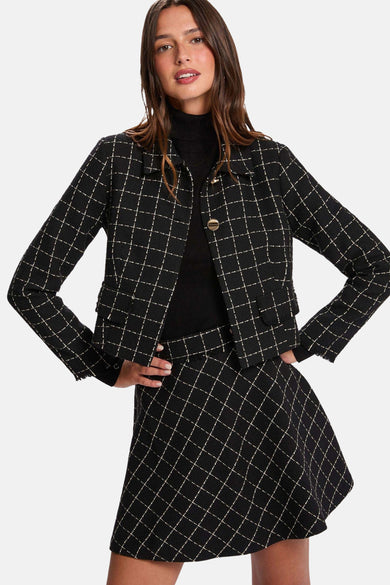 Jupe courte noire de Morgan De Toi, avec un motif à carreaux et portée avec une veste coordonnée et des loafers noirs.