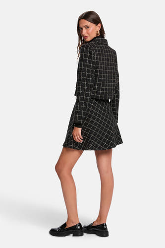 Zwarte korte jas van Morgan De Toi met ruitpatroon, gedragen met rok en zwarte lakleren loafers.
