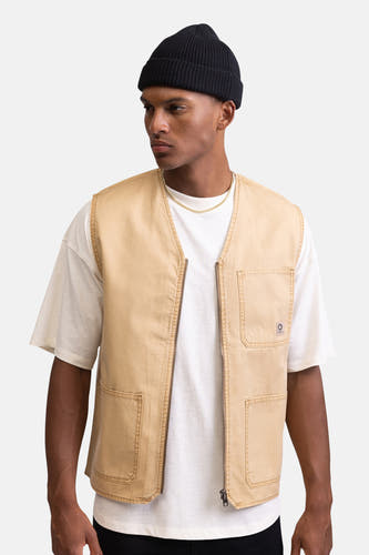 Manteau sans manches beige de REDEFINED REBEL, avec des boutons sur l'épaule, associé à un T-shirt blanc et une beanie noire.
