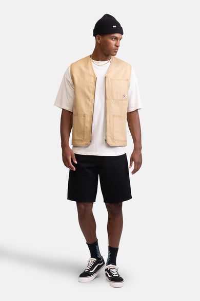 Beige mouwloze jas van REDEFINED REBEL, gedragen over een wit T-shirt, met zwarte shorts en lage sneakers.