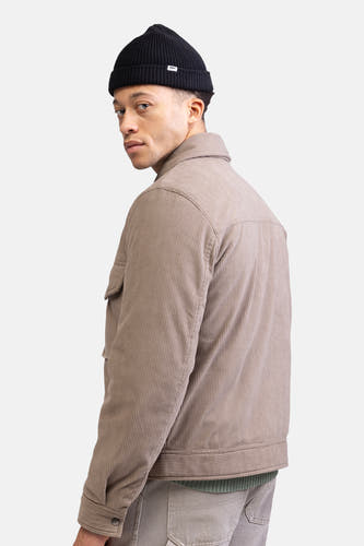 Beige korte jas van REDEFINED REBEL, met corduroy textuur, gedragen met een zwarte muts.
