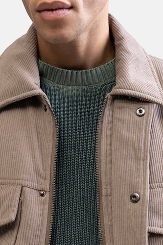 Beige korte jas van REDEFINED REBEL, met een groene gebreide trui eronder en een zichtbare ritssluiting.

