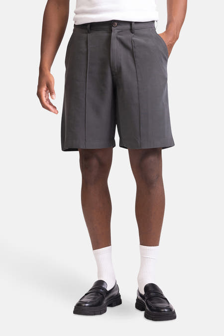 Grijze short van REDEFINED REBEL, met plooien, gecombineerd met een wit T-shirt, witte sokken en zwarte loafers.