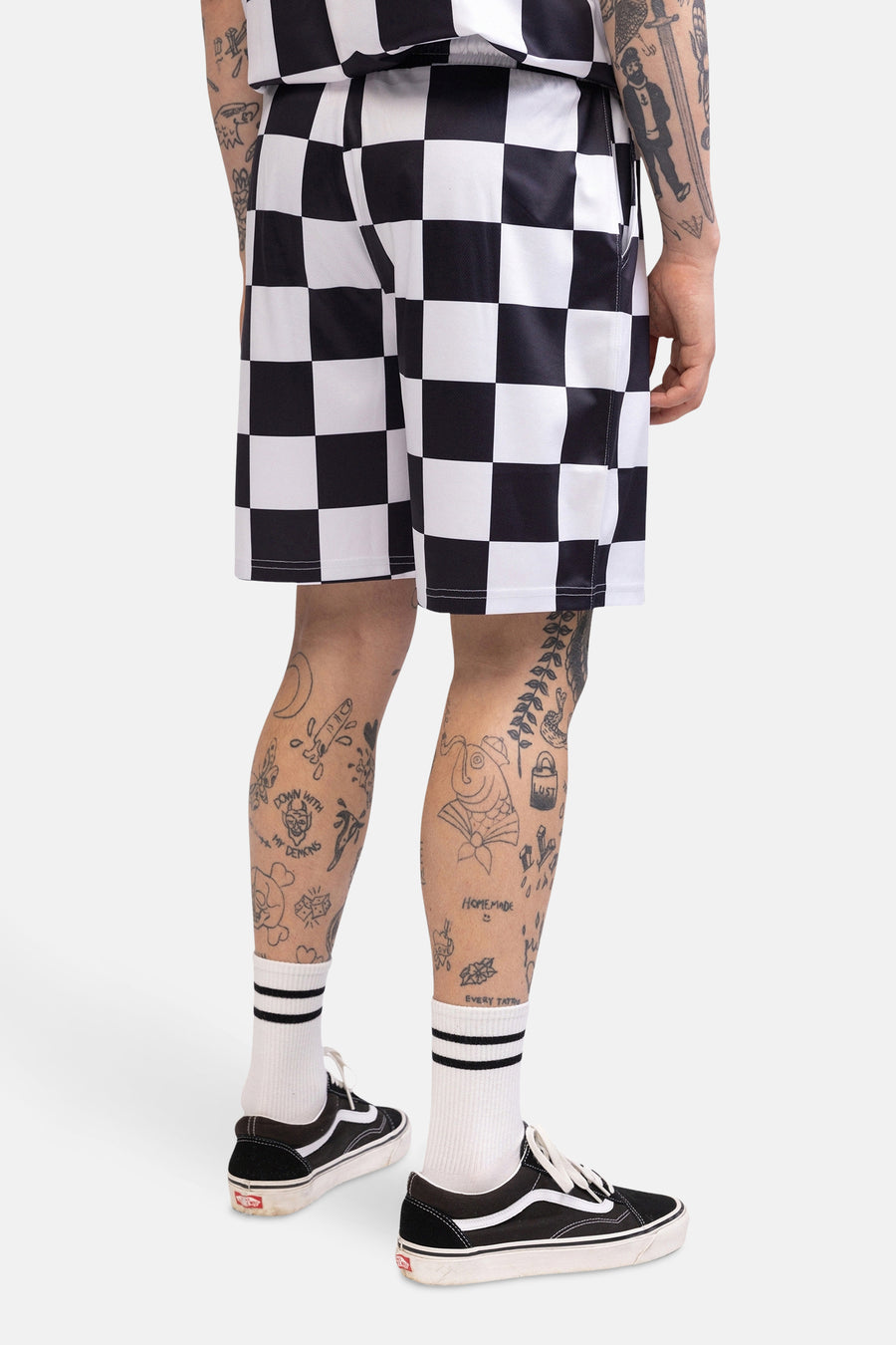 Persoon van achter, geruite broek, sokken met strepen, Vans schoenen, tatoeages.
