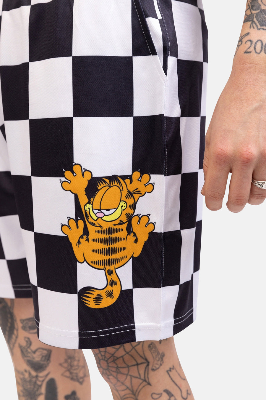 Zwarte en witte geblokte shorts met Garfield print, gedragen door persoon met tatoeages.