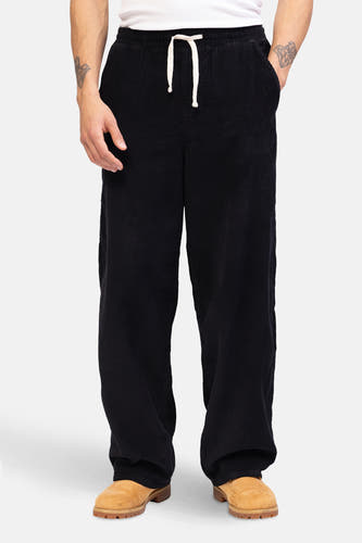Pantalon noir de REDEFINED REBEL, avec une ceinture et une texture rayée, porté avec des chaussures brunes.