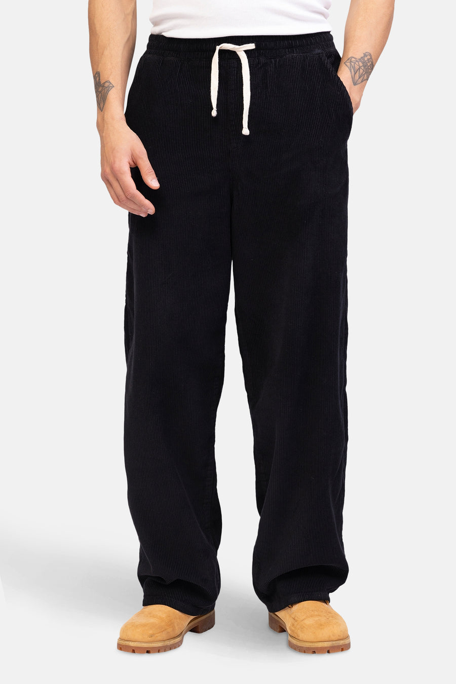 Pantalon noir de REDEFINED REBEL, avec une ceinture et une texture rayée, porté avec des chaussures brunes.