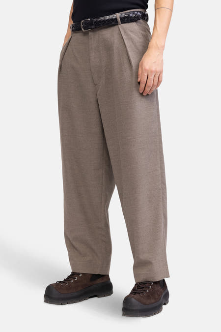 Bruine broek van REDEFINED REBEL, met plooien en een gevlochten riem, gedragen met bruine suède schoenen.
