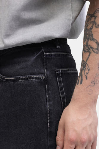 Wijde jeans van donkergrijs denim van REDEFINED REBEL, met witte stiksels en een arm met een tatoeage.
