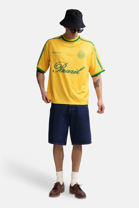 Gele korte mouwen t-shirt met groene accenten en Brazil-print van REDEFINED REBEL, gedragen met donkerblauwe korte broek en zwarte pet, front view.