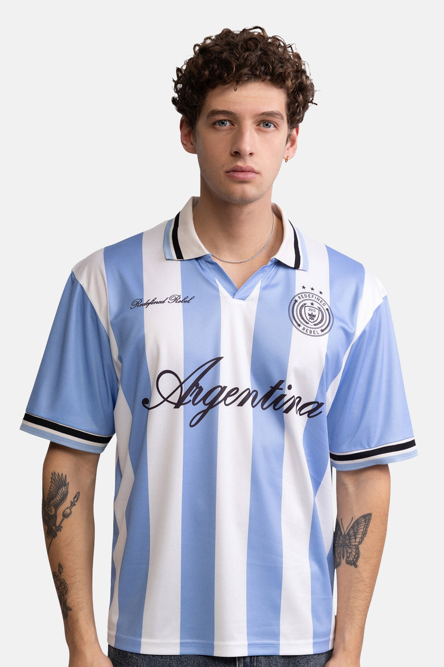 Blauw-wit gestreepte polo van REDEFINED REBEL met 'Argentina' logo en embleem, vooraanzicht model met tatoeages