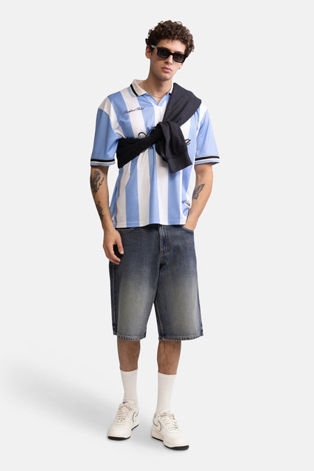 Blauw-witte gestreepte polo van REDEFINED REBEL, met zwart contrast op kraag en mouwen, gedragen met jeansshorts en zonnebril, lifestyle shot.