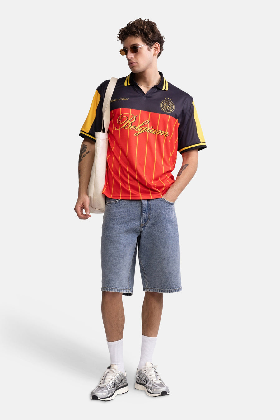 Multicolor polo met rode borst met gele strepen en donkerblauwe mouwen van REDEFINED REBEL, met 'Belgium' in goud en logo, gedragen met jeansshorts en zonnebril.