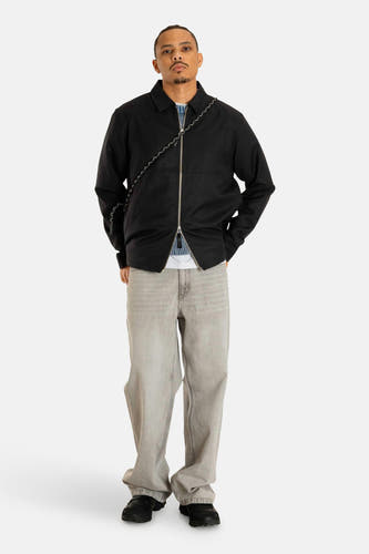 Manteau court noir de WOODBIRD, avec une fermeture éclair argentée et des jeans gris.