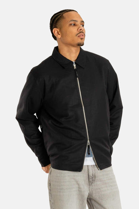 Manteau court noir de Woodbird, avec des manches longues et une fermeture éclair argentée.