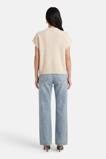 Gilet court sans manches beige de Terra di Siena, avec de larges bretelles, combiné avec un jean bleu et des talons marron.