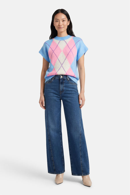 Blauw giletkorte zonder mouw van Terra di Siena, met een ruitpatroon in roze en wit, gecombineerd met donkere jeans en beige laarzen.
