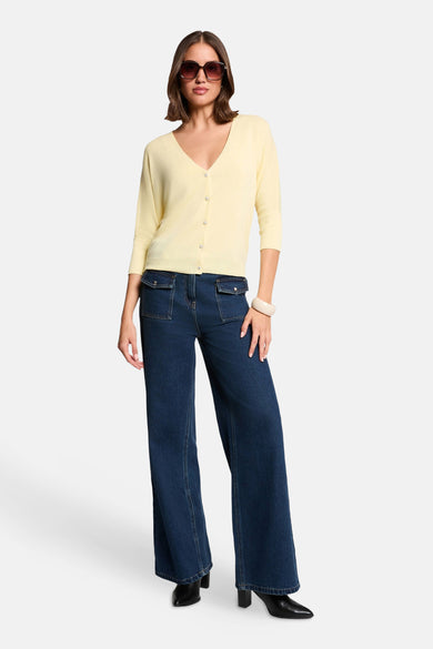 Cardigan jaune Morgan De Toi avec col en V, manches trois-quarts et boutons brillants, porté avec un jean évasé et des lunettes de soleil.
