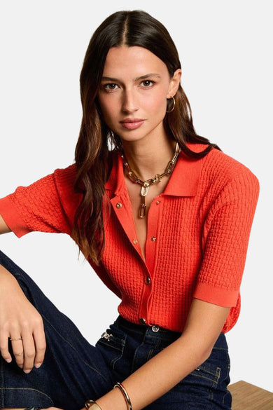 Maillot orange de Morgan De Toi, à manches courtes, associé à des jeans larges et sombres et à des baskets noires.